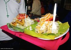 two plates with food on them are sitting on a pink tray in front of a man