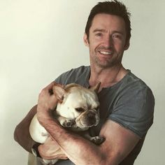 a man holding a small dog in his arms and smiling at the camera while wearing a gray shirt