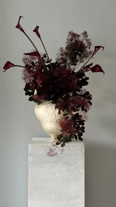 a vase filled with flowers on top of a white table next to a gray wall