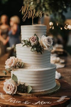 a white wedding cake with flowers on top and the word mr and mrs spelled in cursive