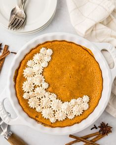 an overhead view of a pumpkin pie with white flowers on top and cinnamon sticks in the background