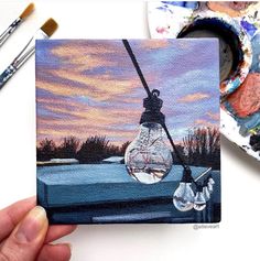 a painting of a light bulb hanging from a wire with paintbrushes next to it