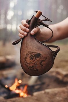 a person holding a leather bag with a wolf design on it and a campfire in the background