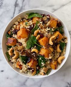 a white bowl filled with rice, nuts and spinach on top of a marble table