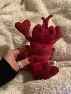 a hand holding a red stuffed animal on top of a white bed covered in blankets