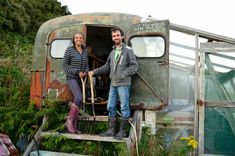 two people standing in the doorway of an old trailer with plants growing out of it