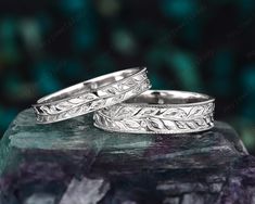 two silver wedding rings sitting on top of a rock next to another ring with leaves