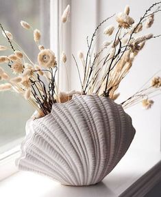 a vase with dried flowers in it sitting on a window sill