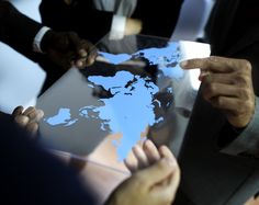 several people pointing at a world map on a tablet