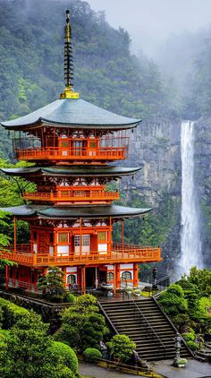 an orange pagoda with stairs leading up to it and a waterfall in the background, surrounded by lush green trees