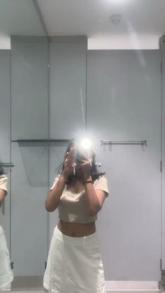 a woman taking a selfie in front of a mirror while wearing a white skirt