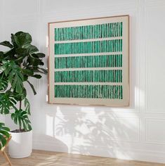 a large green painting hanging on the wall next to a potted plant in a white room