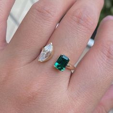 a woman's hand with a green and white diamond ring on top of it