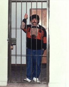 a man is standing behind bars in a jail cell holding his fist up and looking at the camera