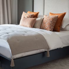 a bed with white and orange pillows on top of it's headboard in a bedroom