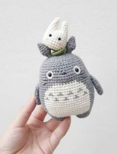 a hand holding a small crocheted totoro with a stuffed animal on top of it