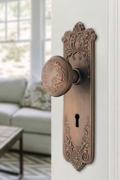 an ornate door handle on the side of a white wall with a couch in the background