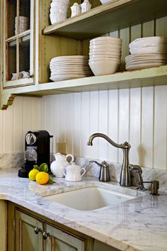 a kitchen with marble counter tops and white dishes on wooden shelves above the sink,