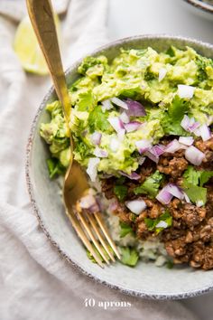 a white bowl filled with meat and veggies on top of a table next to a fork