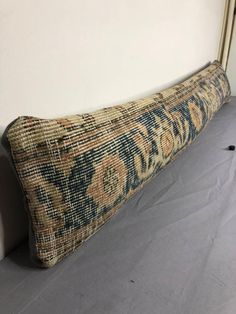 an old rug is laying on the floor in front of a white wall with a gold frame