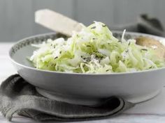 a white bowl filled with shredded cabbage on top of a table next to a knife