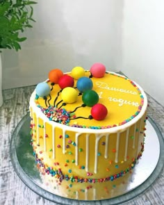 a birthday cake decorated with balloons and sprinkles sits on a table next to a potted plant