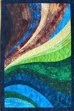 a quilted wall hanging on the side of a wooden fence with blue, green and yellow colors