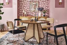 a dining room with pink walls and wooden table surrounded by chairs in front of a floral wallpaper