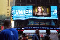 people are walking around in front of a building with an advertisement on it's side