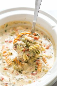 a spoonful of pasta and vegetable soup in a white bowl with a silver spoon