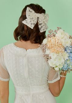 a woman in a white dress holding a bouquet of flowers and wearing a large bow