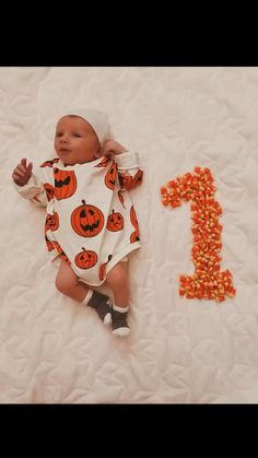 a baby laying on top of a bed next to the numbers 1 and pumpkins