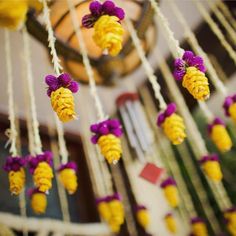 yellow and purple flowers hanging from strings in a room with a chandelier behind them