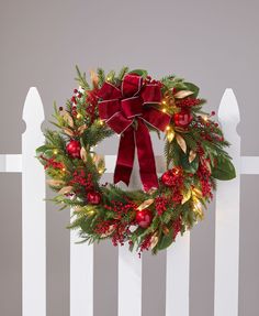 a christmas wreath on a white fence with red bows and lights hanging from it's sides