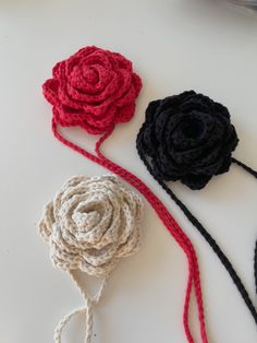 three crocheted flowers on a white surface with red, black and gray yarn