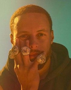 a man holding two silver coin rings to his face and looking at the camera while wearing a black hoodie