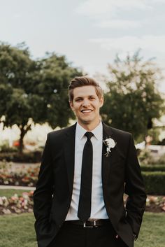 a man wearing a suit and tie standing in front of some flowers on the grass