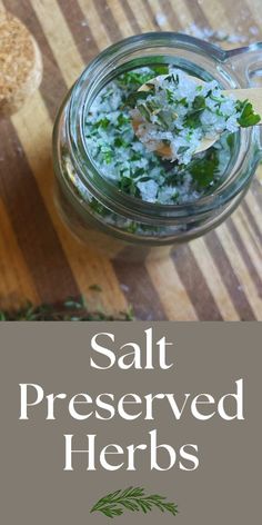 a jar filled with salt and herbs on top of a wooden table next to a spoon