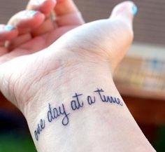 a woman's wrist with the words one day at a time tattooed on it