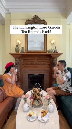 two people sitting on couches in front of a fire place with tea and pastries