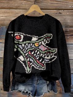 a black sweater with an embroidered wolf on the front and back, hanging against a wooden wall