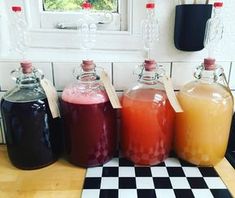 four different colored drinks in glass jugs sitting on a checkerboard counter top