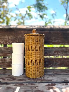 two rolls of toilet paper sitting next to a wicker basket on a wooden bench