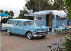 an old blue car parked in front of a camper trailer with awnings