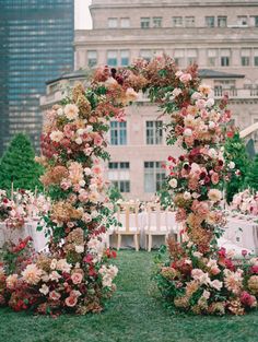 an outdoor ceremony setup with flowers and greenery on the grass in front of tall buildings