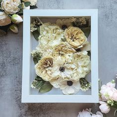 an arrangement of flowers in a white frame on a gray surface next to some pink and white flowers