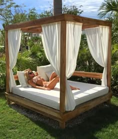 a woman laying on top of a white bed in the grass next to some trees