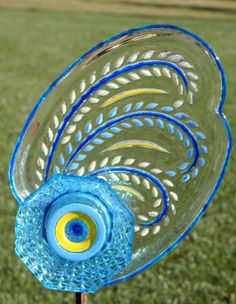 a blue and yellow glass bird on top of a wooden stick with grass in the background