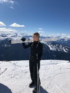 a woman standing on top of a snow covered slope holding skis in her hands