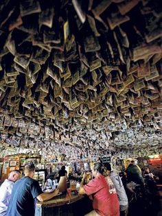 several people sitting at a bar with money hanging from the ceiling above them and on the wall